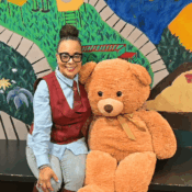 Alicia Powell, Program Director of ECEAA, pictured in front of a colorful mural next to a fluffy, life-size teddy bear.